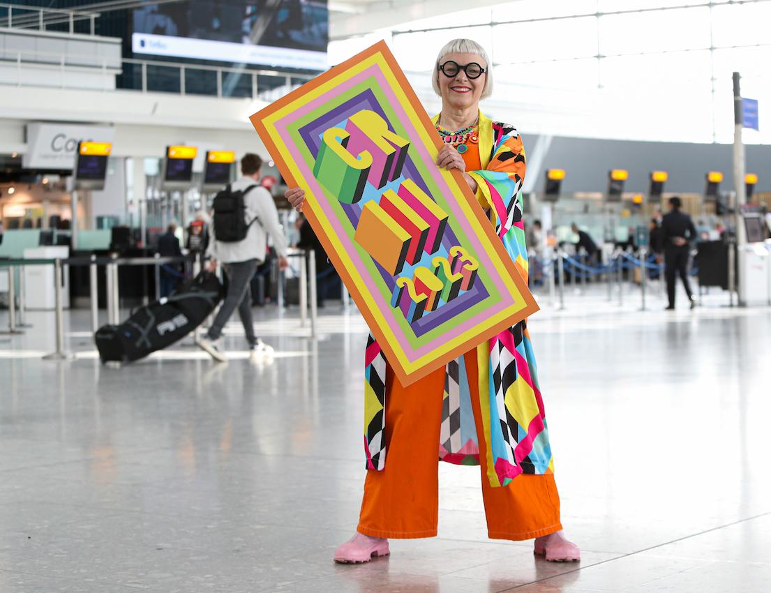 Download Image - Commemorative luggage tags for the Coronation of King Charles III commissioned by Heathrow and designed by Morag Myerscough. Artist featured in photo.  picture