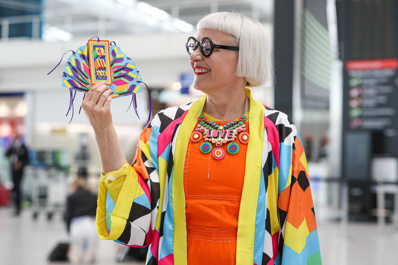 Commemorative luggage tags for the Coronation of King Charles III commissioned by Heathrow and designed by Morag Myerscough. Artist featured in photo. 